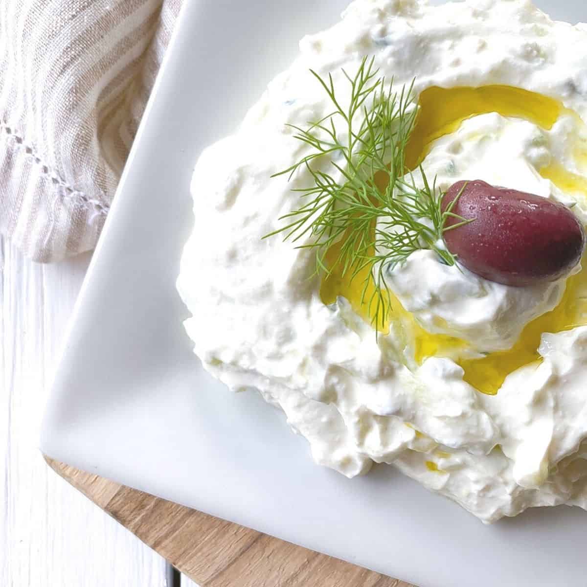 greek yogurt tzatziki dip on a plate with olive oil and olive.