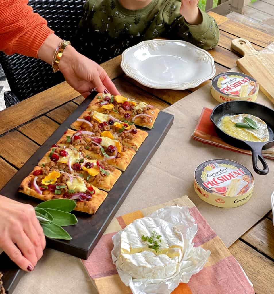 Placing a board with pumpkin flatbread on outdoor table.