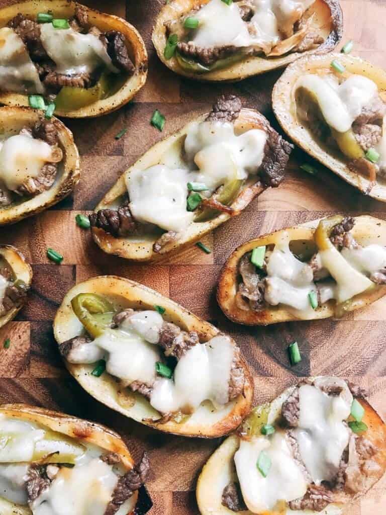 potato skins stuffed with cheese and peppers and steak on cutting board.
