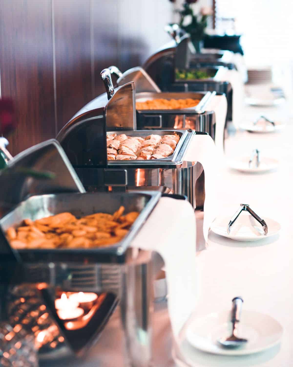 chafing dishes on buffet table with food inside