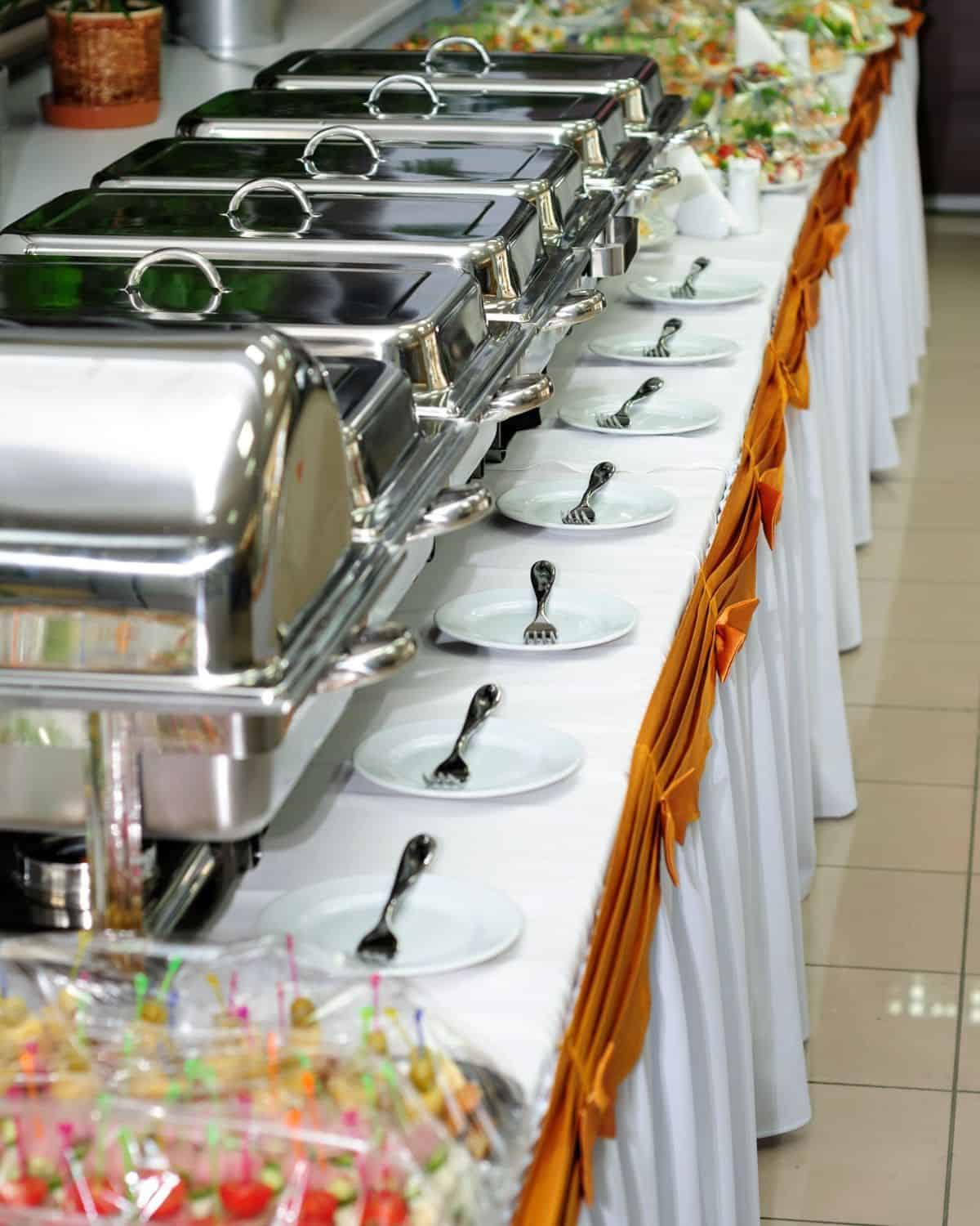 a buffet station set up with chafing dishes on a long table.