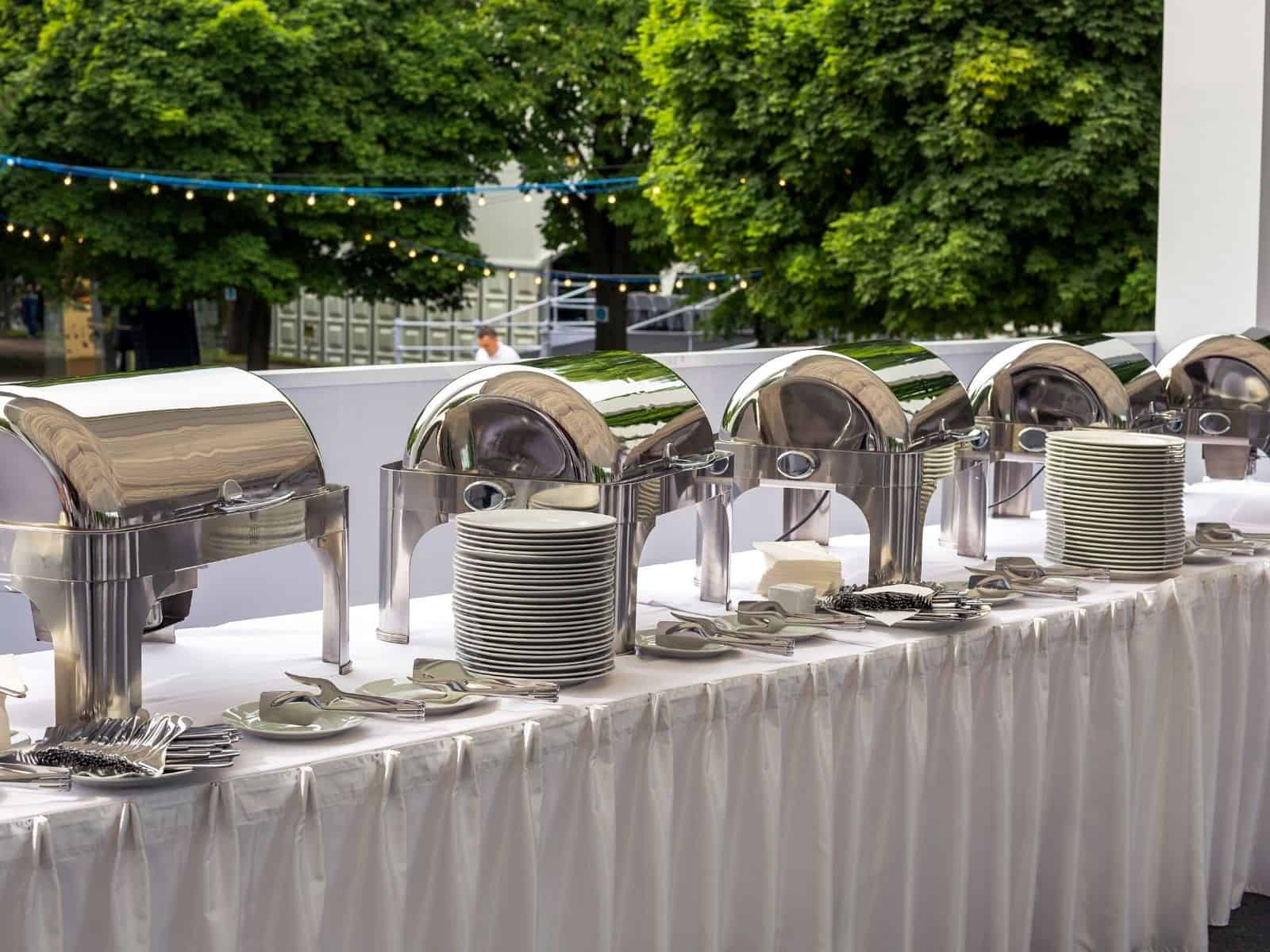 chafing dishes on a long buffet table with plates.