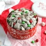 No peanut butter puppy chow in a Christmas tin on table with red and green colors.