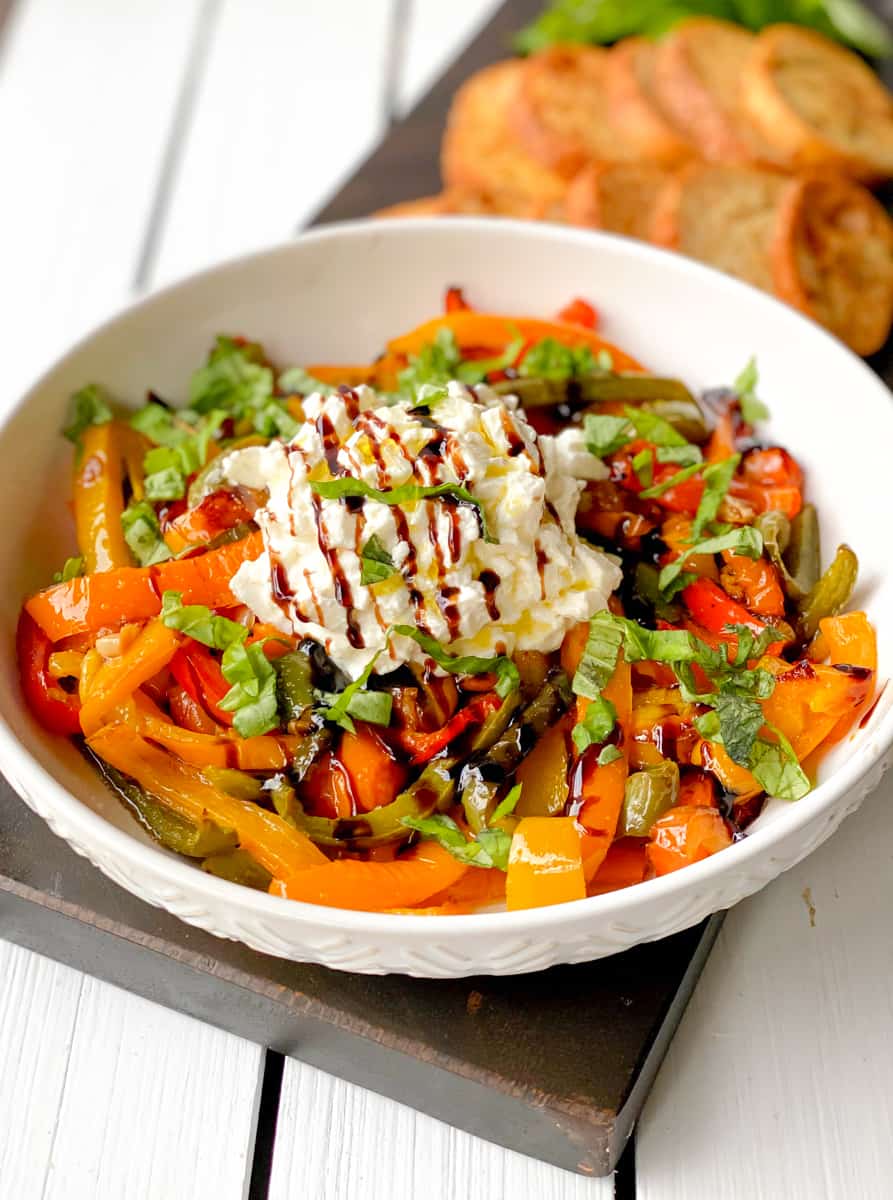 Burrata mozzarella ball with balsamic glaze and roasted peppers in a bowl.