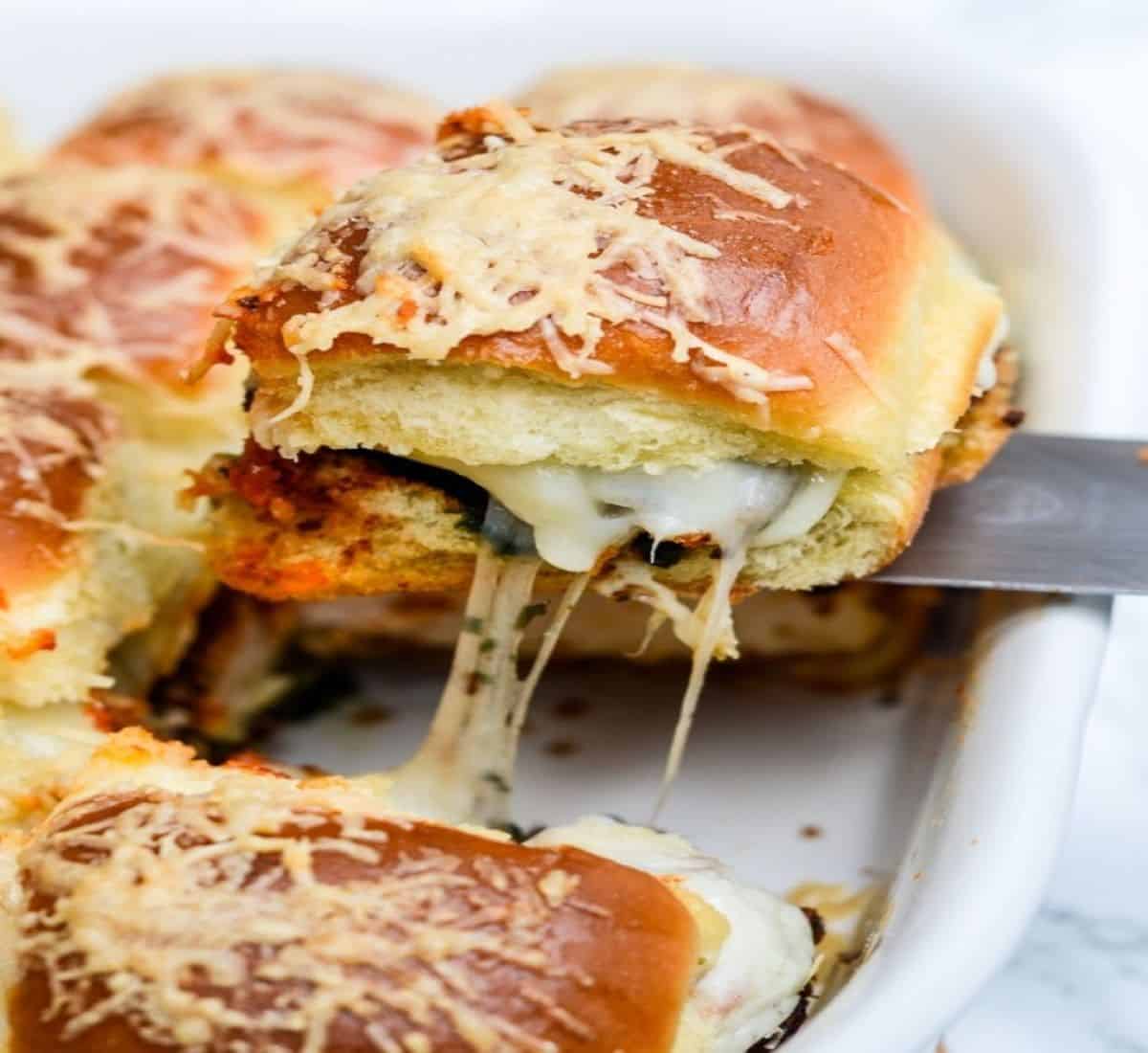 mini chicken parm pesto slider being pulled out of casserole dish.