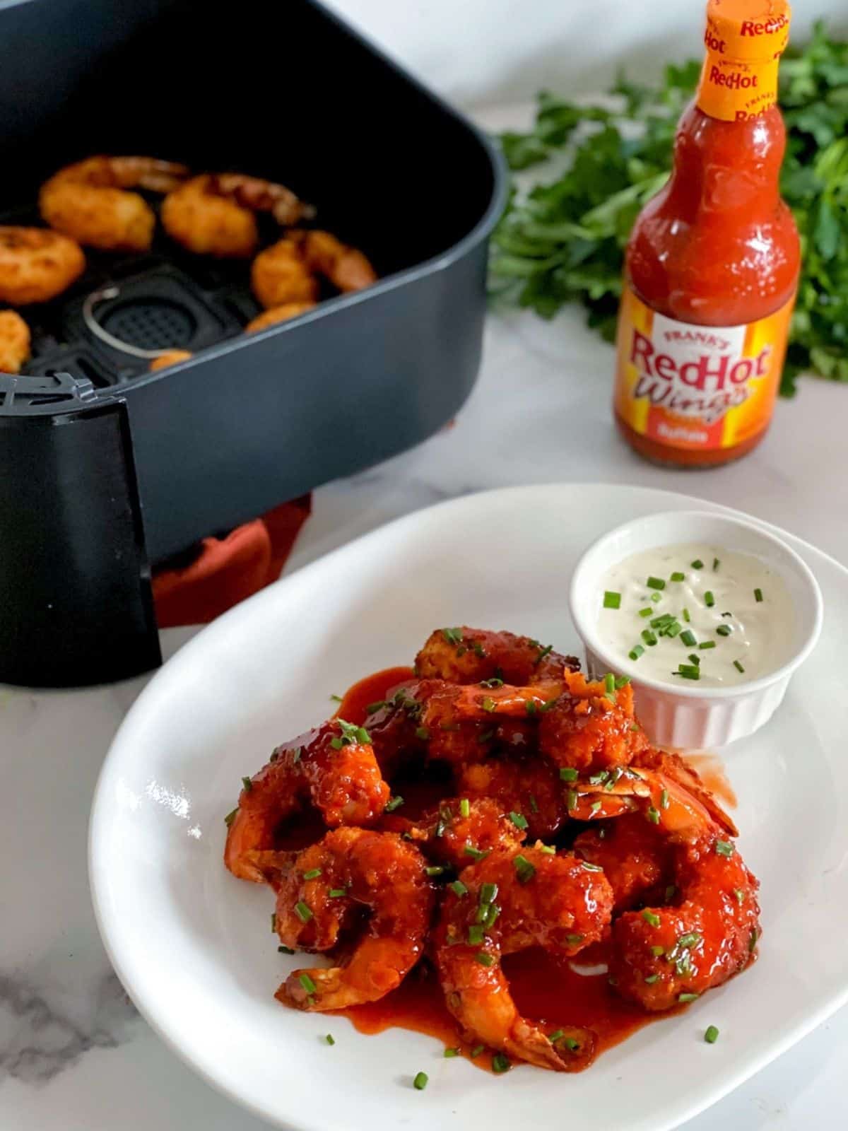 Air fryer buffalo shrimp on a plate with Frank's hot sauce in the background.