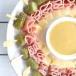 skewered ham cheese and pickle appetizer on a plate with dipping sauce in center.