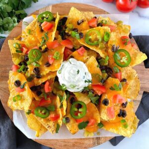 air fryer nachos with cheddar cheese, beans, tomatoes and sour cream on plate.