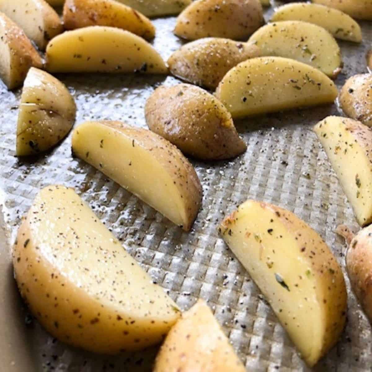 Rodajas de patata al horno sazonadas en una bandeja para hornear.