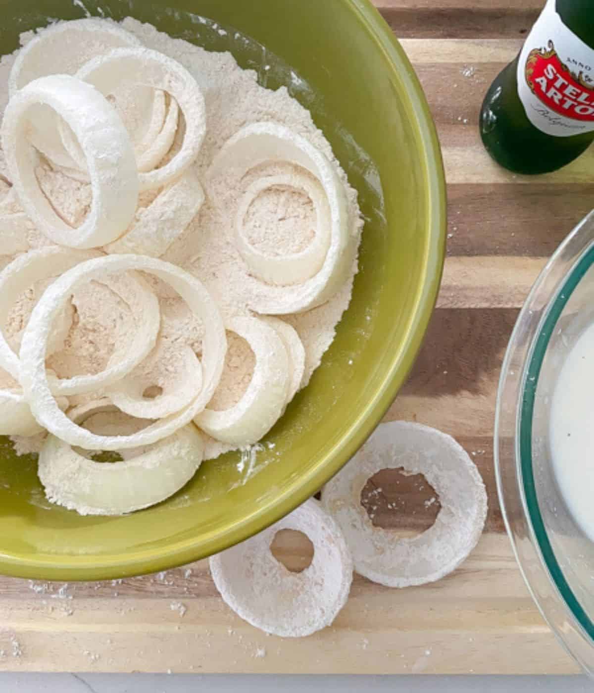 sliced onion rings in flour on a cutting board with a beer bottle.