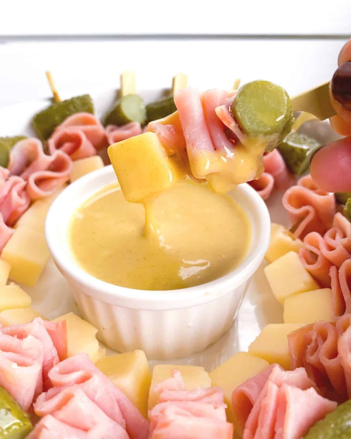 ham, swiss and pickles skewered on a stick dipping into sauce.