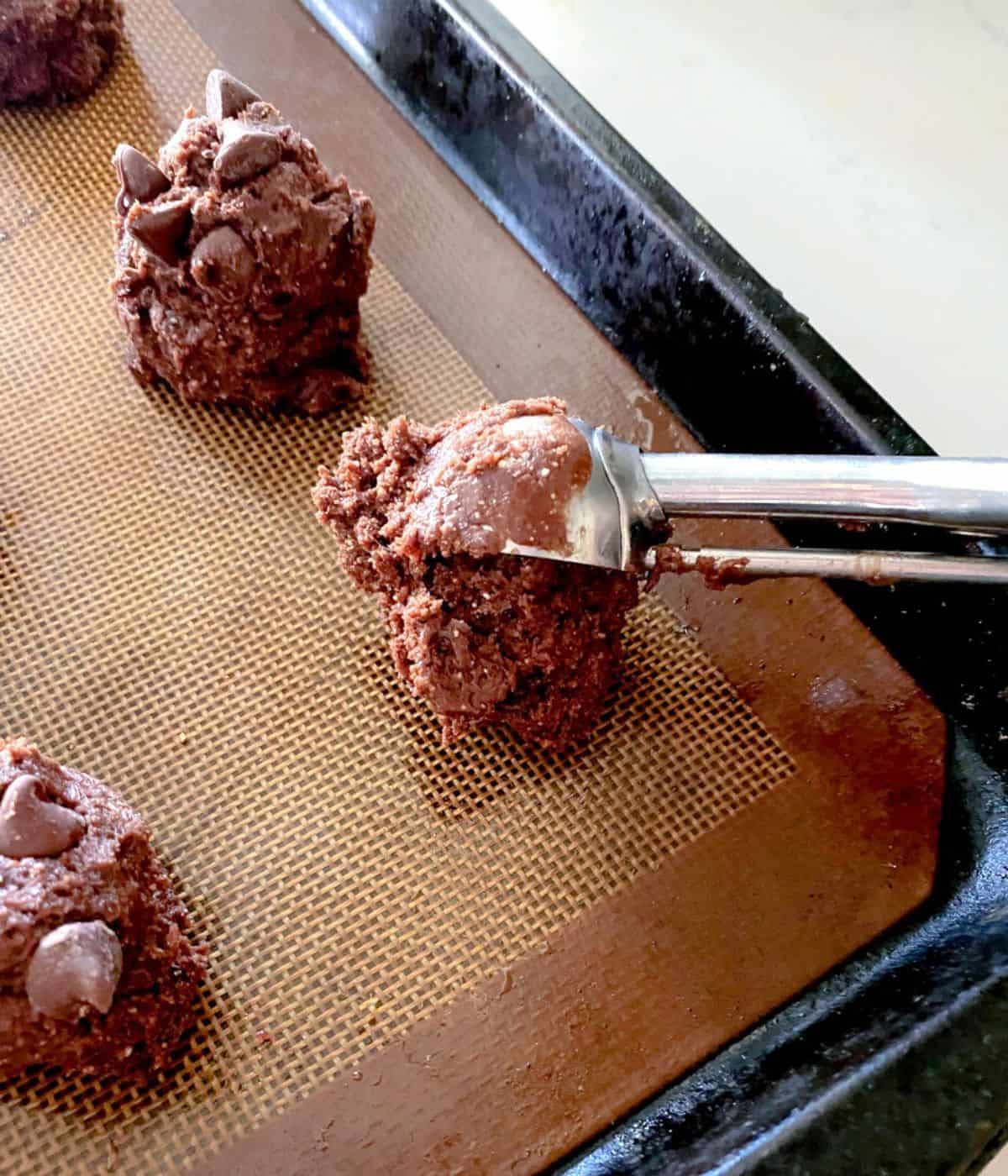 chocolate chip cake batter cookies being scooped onto nonstick baking sheet.