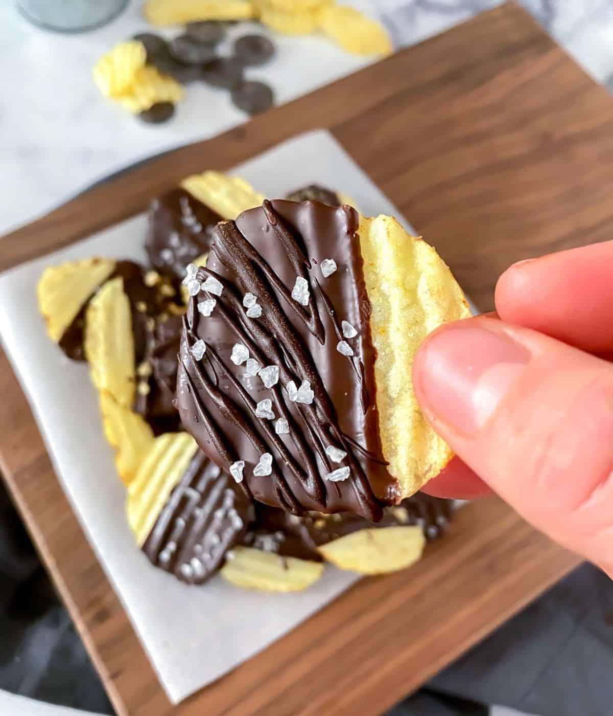 Holding up a chocolate covered ruffled potato chip coated with sea salt.