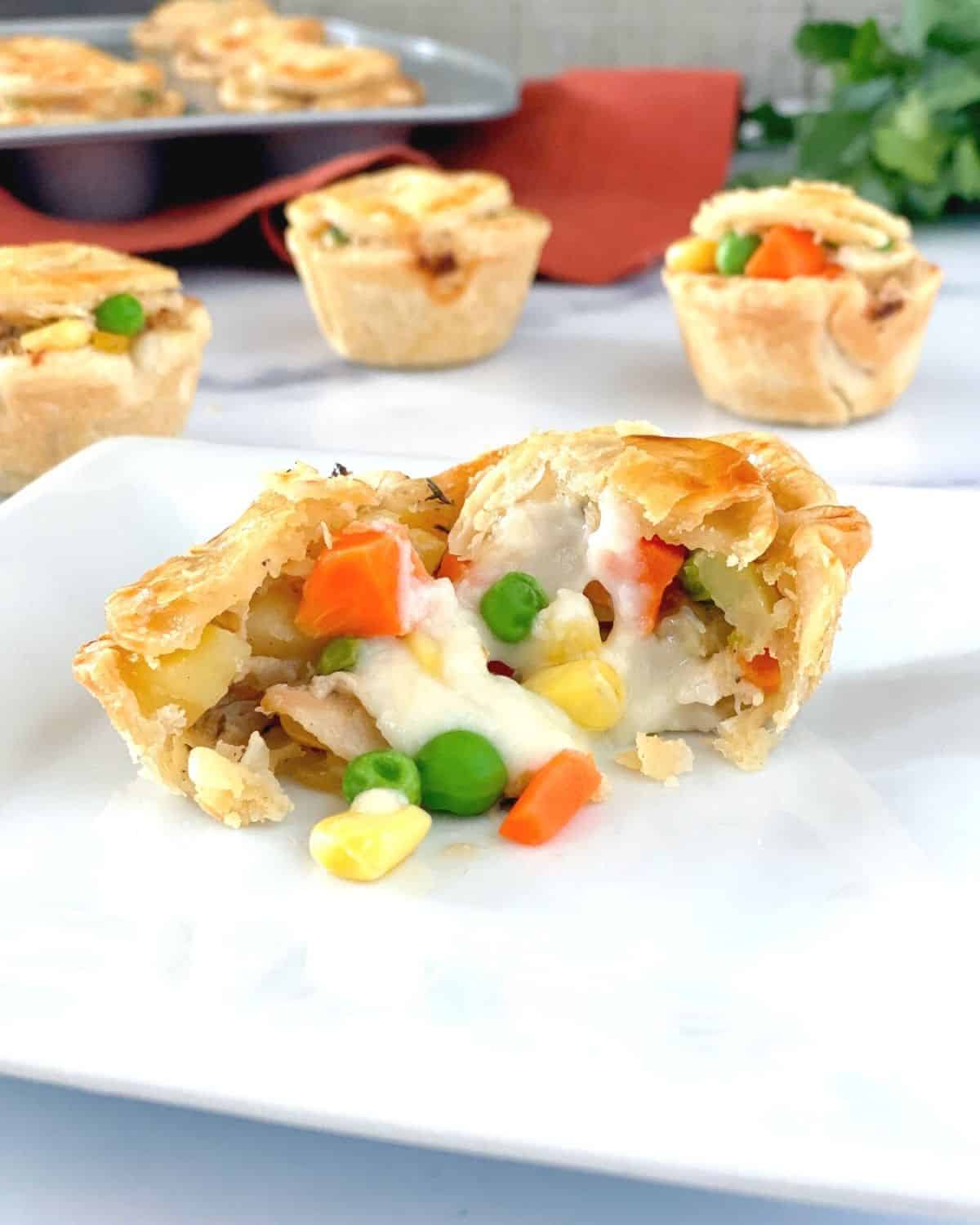 The inside of a mini chicken pot pie on a plate with veggies spilling out.