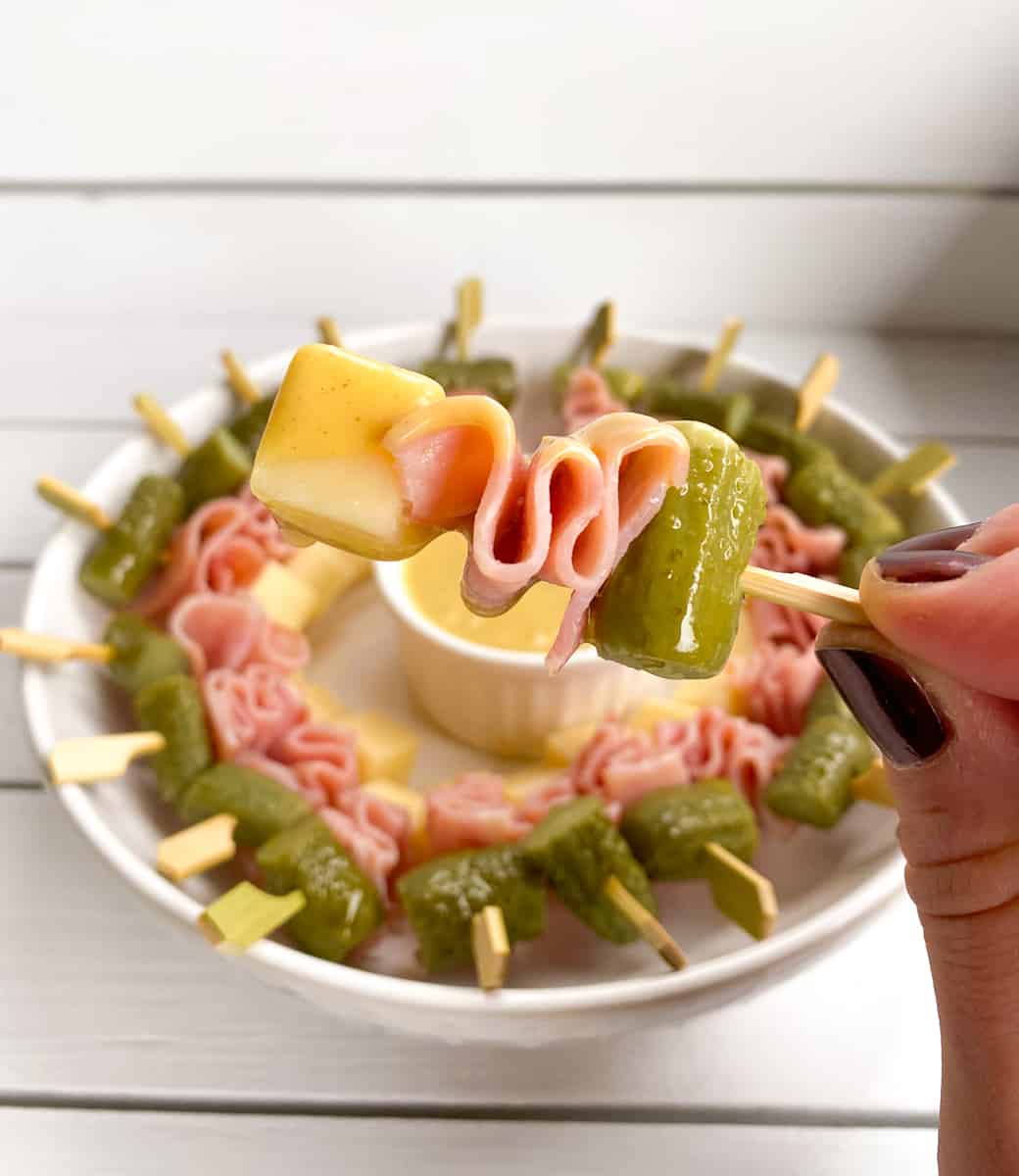 holding up skewered ham cheese and pickle appetizer on a stick.