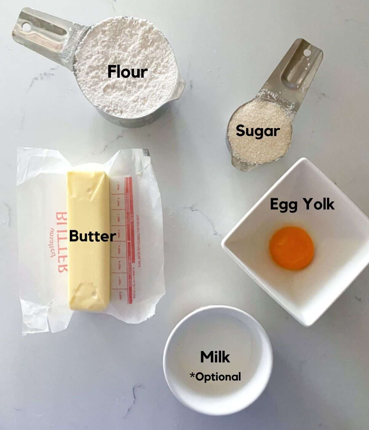 Egg custard tartlet dough ingredients on a table including flour, sugar, butter, egg yolks and milk.