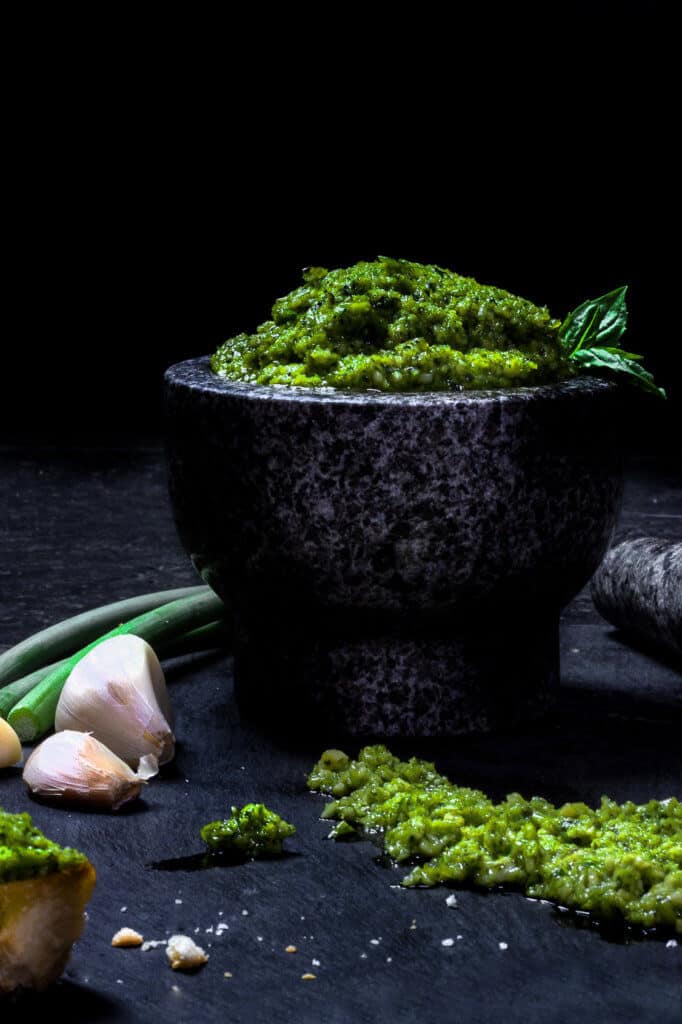 green garlic scape pesto in a mortar with garlic on the side.