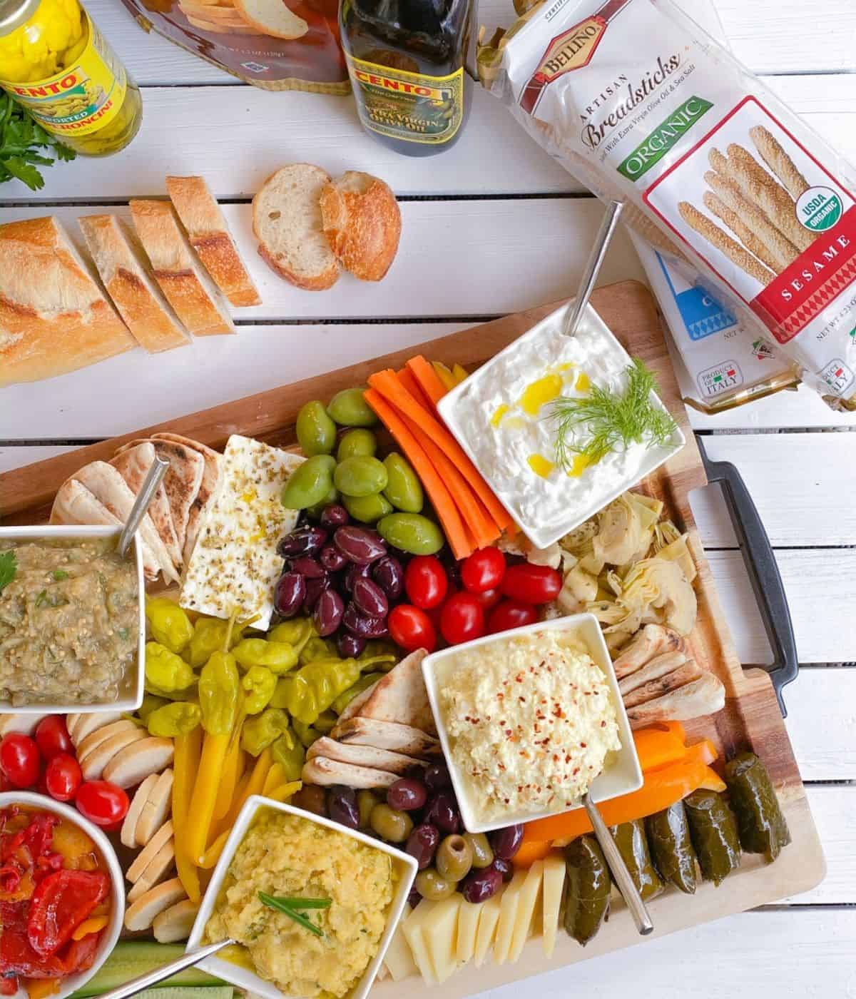 Greek mezze appetizers on a wooden cutting board with spreads and dips.