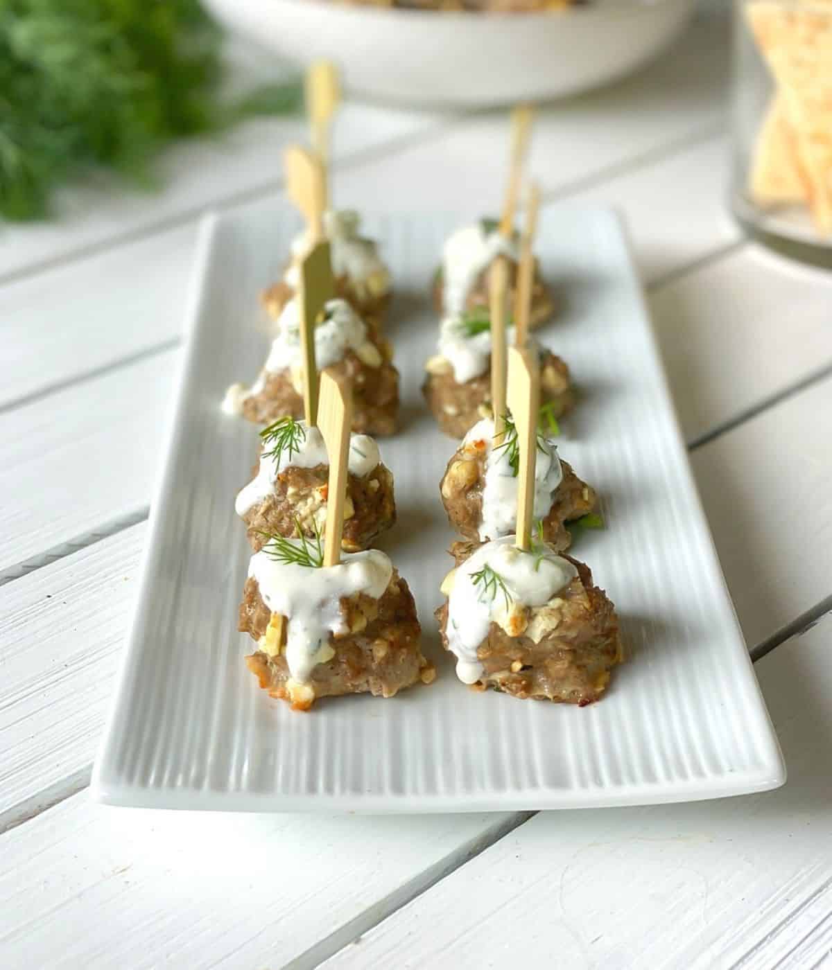 Skewered lamb and feta cheese meatballs on a plate with tzatziki sauce.