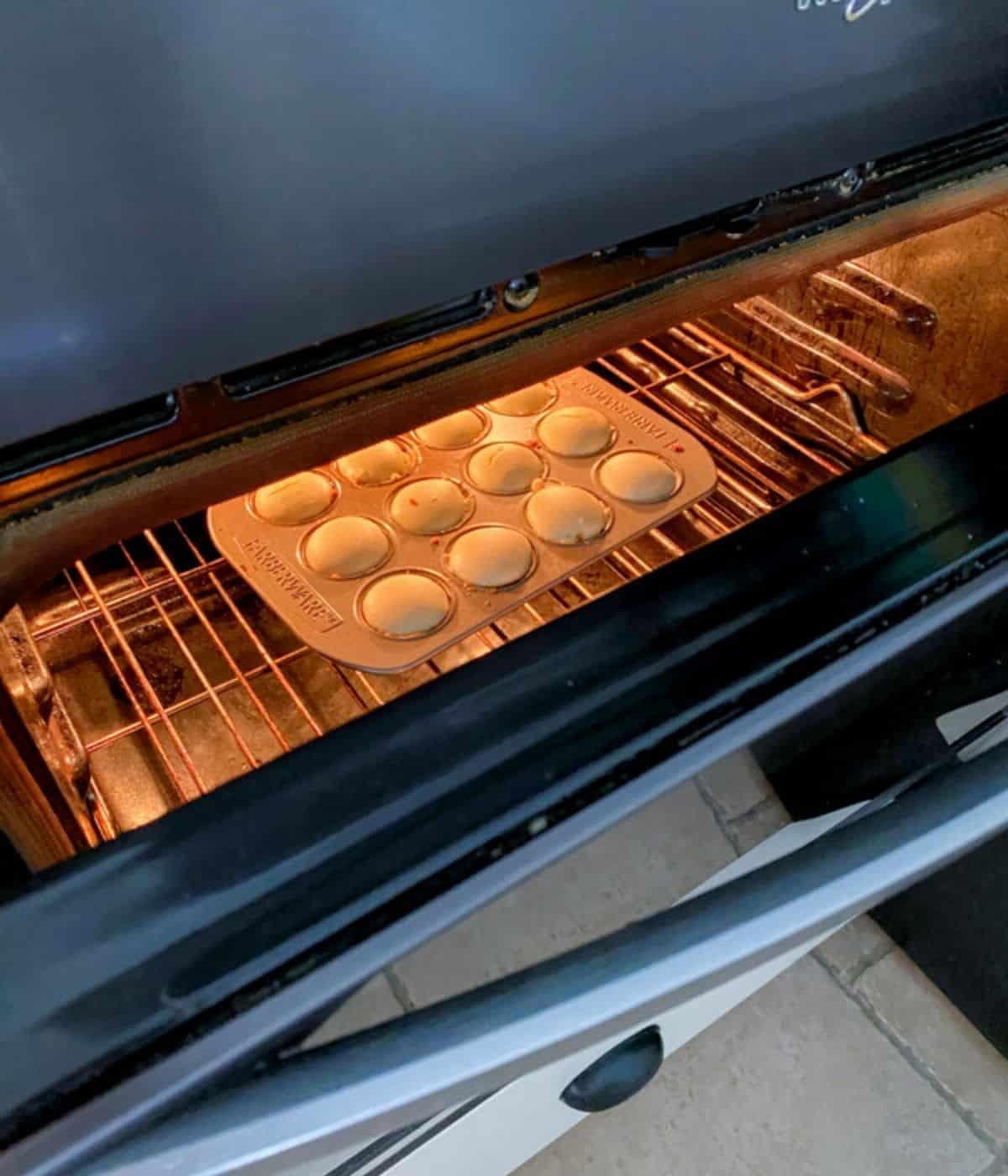 oven cracked open with mini cheesecakes inside.
