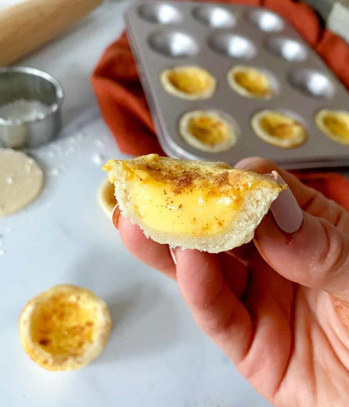 Hand holding a mini egg custard tartlet cut in half.