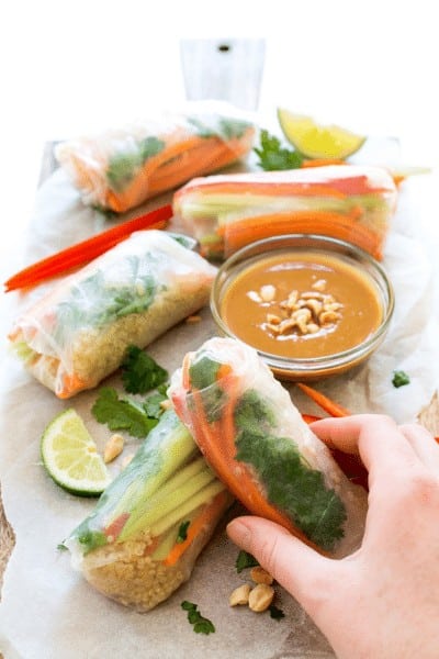 4 spring rolls on a wrapper with a clear bowl of peanut dipping sauce and a lime wedge garnish. 