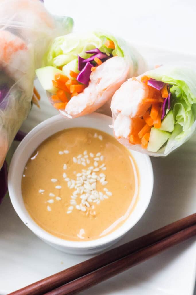  A spring roll cut in half sitting on the edge of a white bowl filled with dipping sauce. 