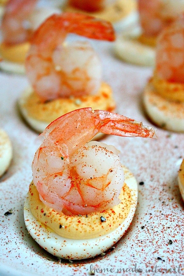 Deviled eggs with shrimp on top with spices sprinkled over them on a white tray.