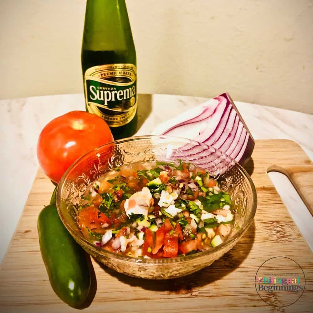 Ceviche in a crystal bowl on a wooden cutting board with a tomato and a jalapeno pepper.
