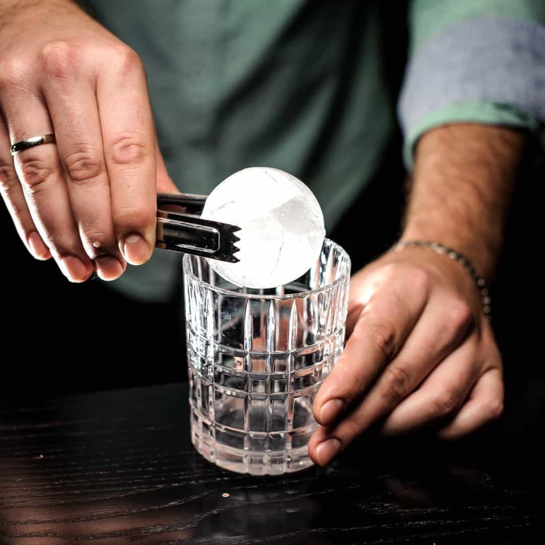 Bartender placing ice ball into cocktail.