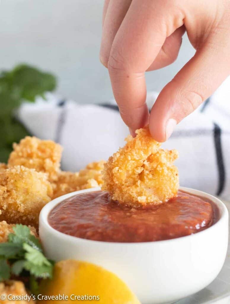 Fried shrimp dipped in a bowl of cocktail sauce.
