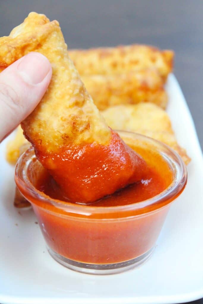 Shrimp egg roll being dipped in sauce.