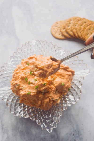 Crystal bowl full of shrimp dip with a silver spoonful of dip.