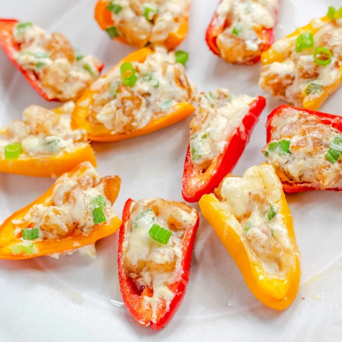Red and yellow mini peppers filled with shrimp rangoon filling laying on a white plate. 