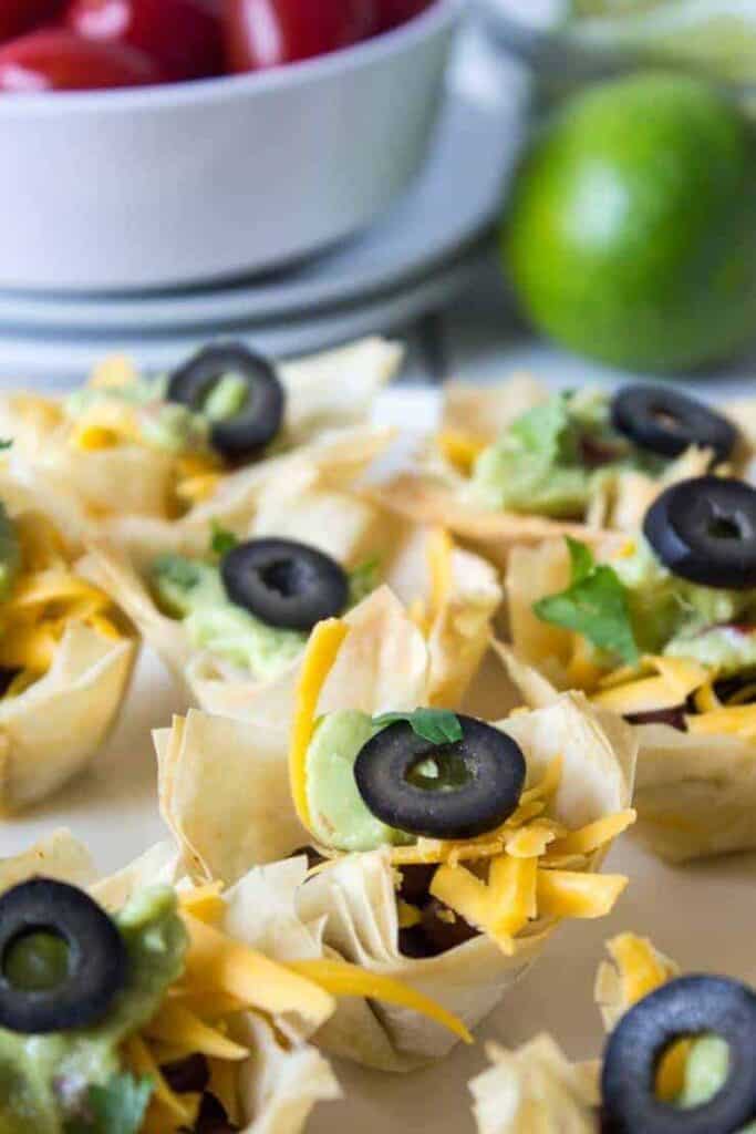 Close up of a Black Bean Taco cup with guacamole and shredded cheese with a slice of black olive on top.