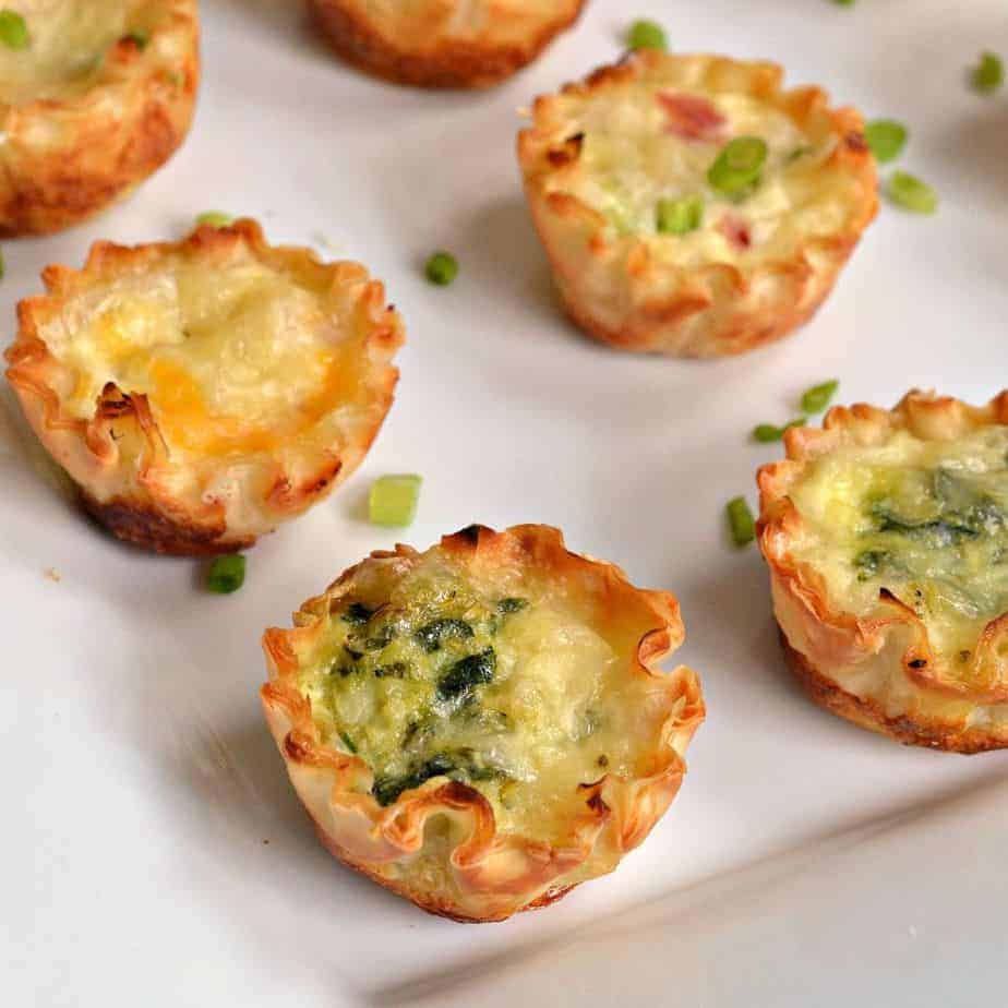 Four mini quiche on a white surface and garnished with green onions. 