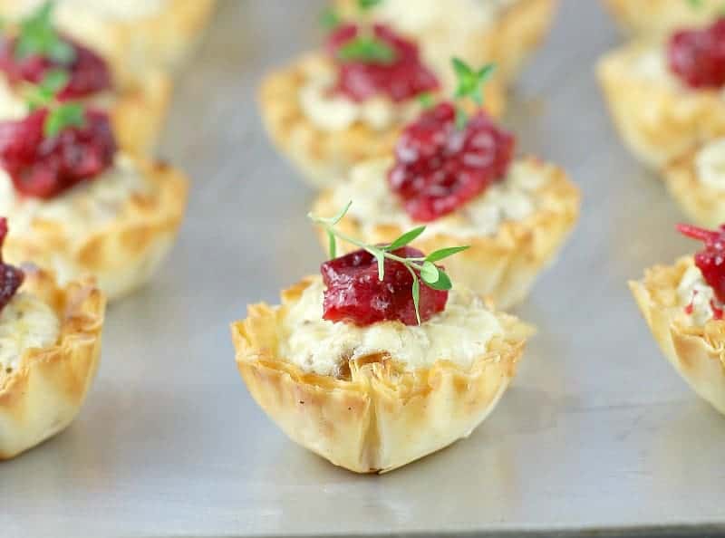 Rows of mini tarts with cranberry mango compote on top and a sprig of fresh thyme. 