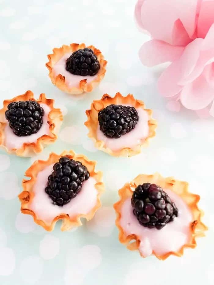 Five blackberry yogurt tarts with a pink flower in the corner. 
