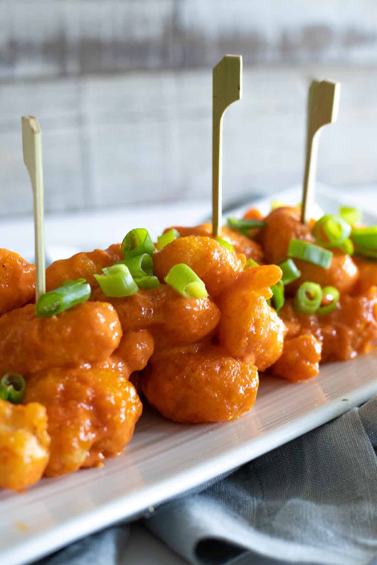 Dynamite shrimp appetizer skewered with scallions on a plate.