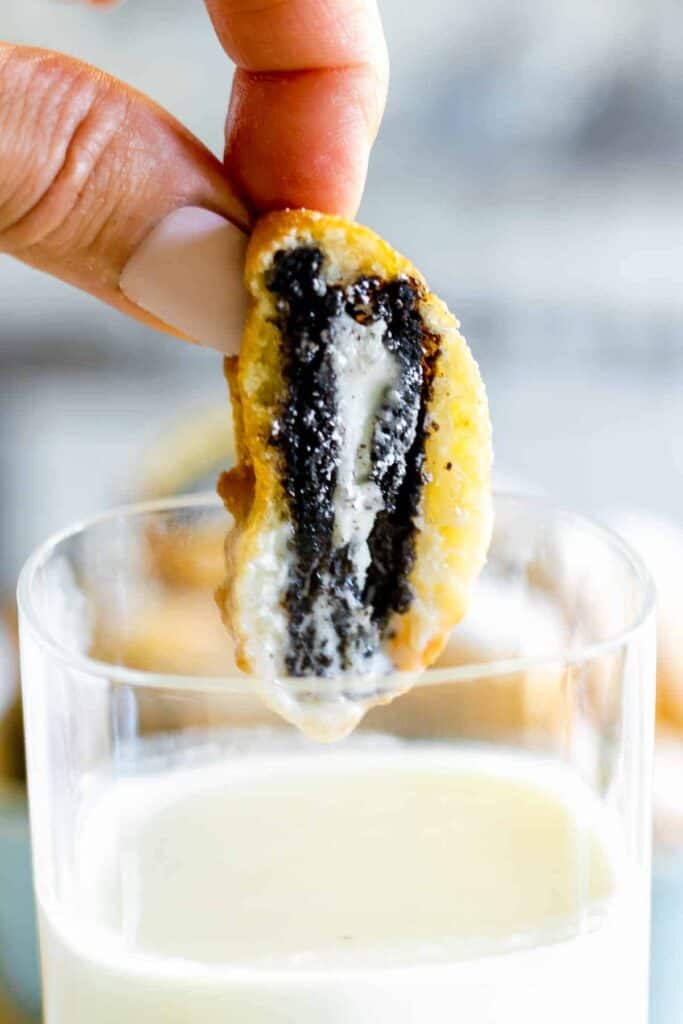 Deep fried Oreo being dipped into milk