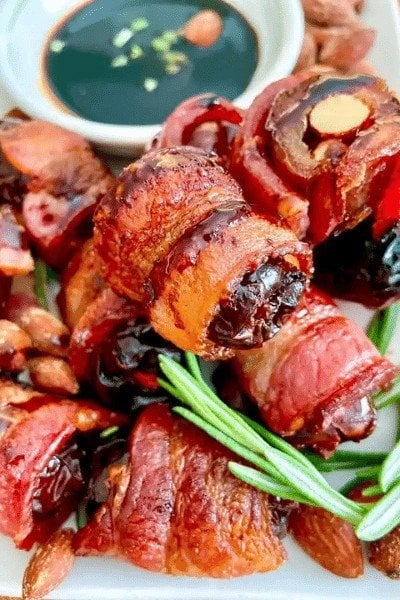 A pile of bacon wrapped dates with a close-up of the top one with a green garnish. 