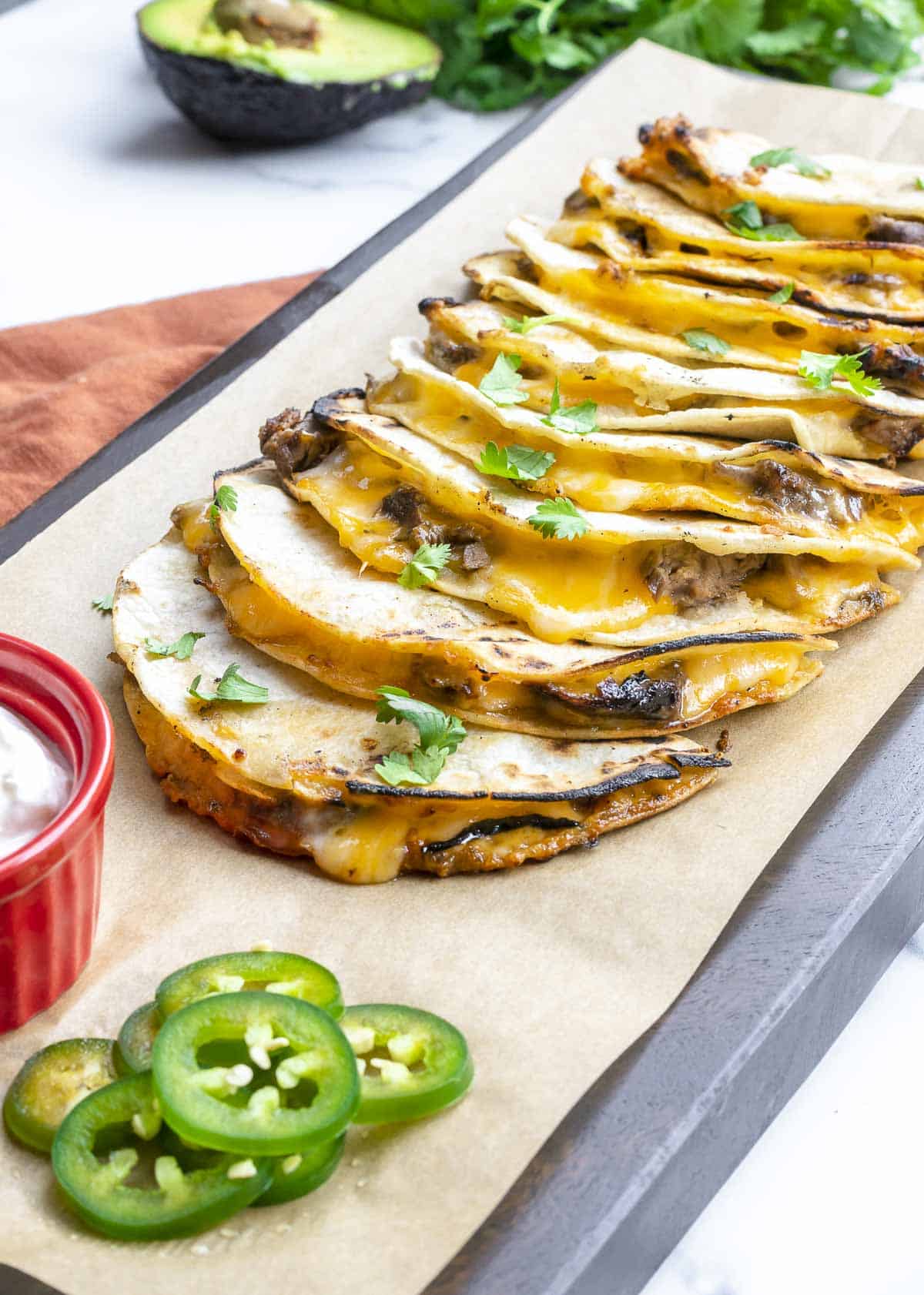 Carne asada skirt steak quesadillas made with corn tortillas served on a long cutting board with jalapeno slices.