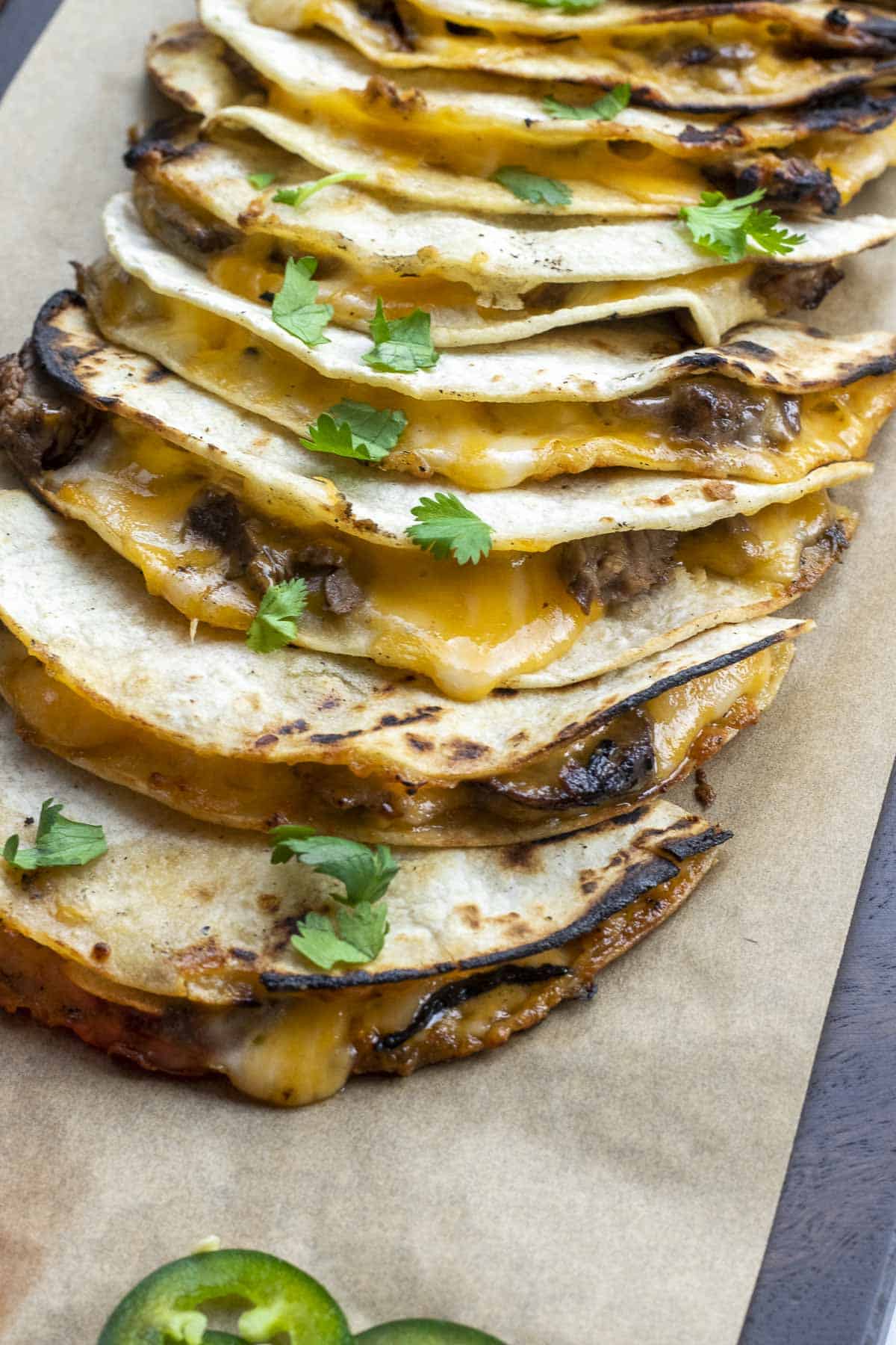 Corn tortilla carne asada mulitas on a cutting board layered with cilantro on top.