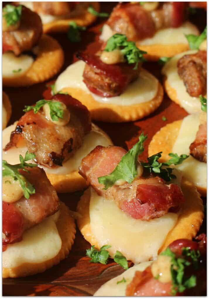Bacon-wrapped chicken on a cracker with melted cheese and a green garnish. 