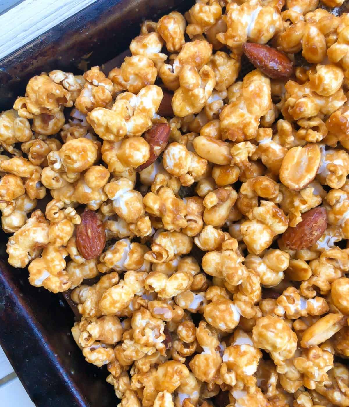 Closeup of caramel popcorn with peanuts and almonds on a baking sheet.