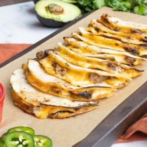 Carne asada mulitas on a cutting board with jalapenos and avocado.