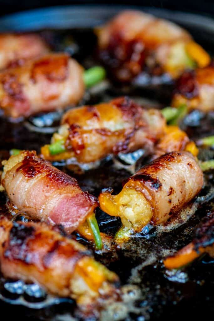 Grilled bacon-wrapped tater tot bombs sizzling in a skillet.