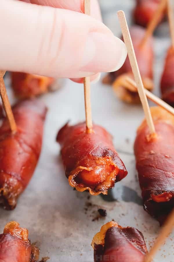 Close up of a bacon wrapped little smokie being held with a toothpick.