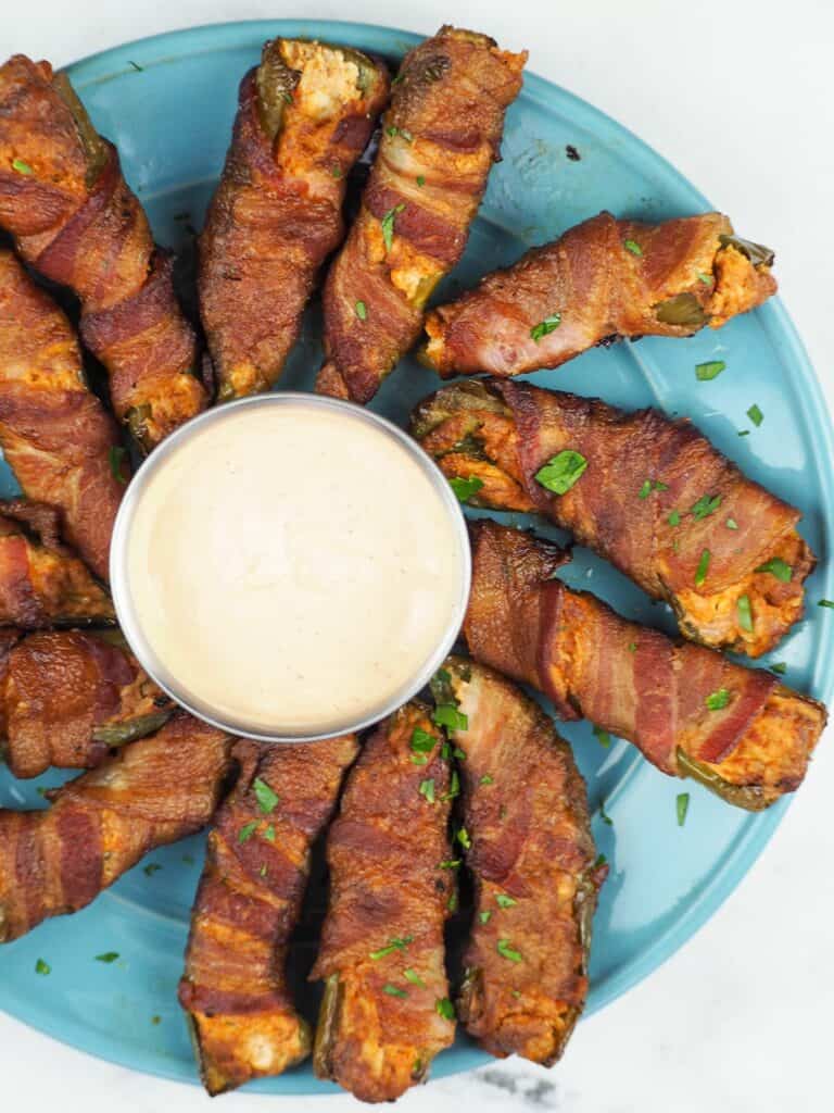 Jalapeno poppers on a round blue plate with a small bowl of dipping sauce in the middle.