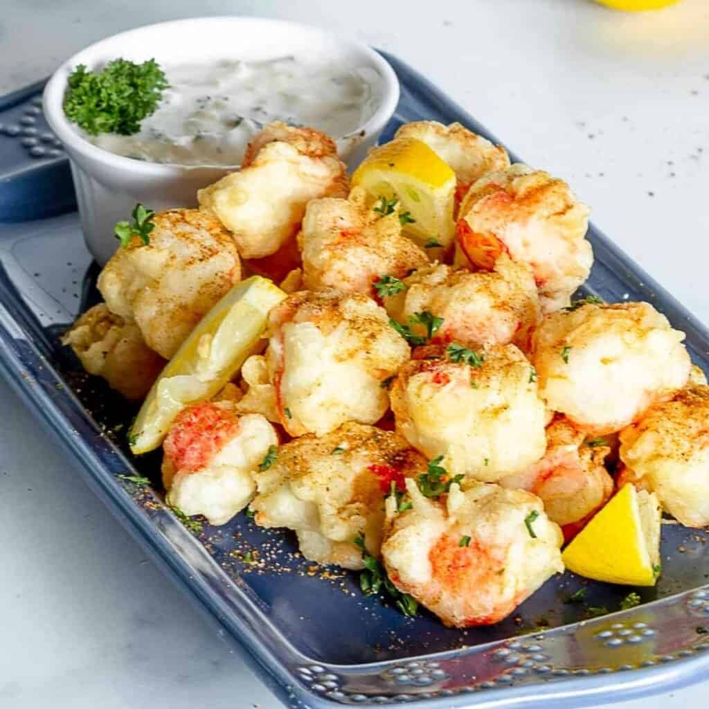 Fried crab stick bites on plate with seasoning and lemons.